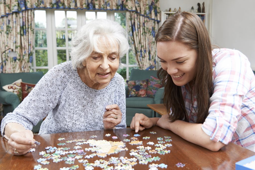 Teenage Granddaughter Helping Grandmother With Jigsaw Puzzle
