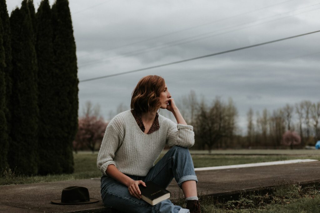 A woman sitting on a gravel path looking off into the distance, deep in thought.