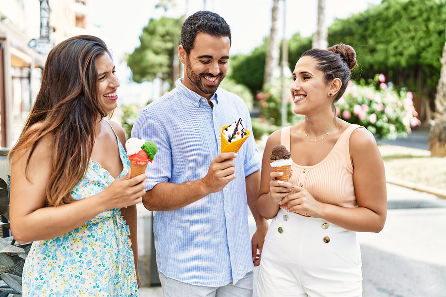 three people smiling and holding food like ice cream
