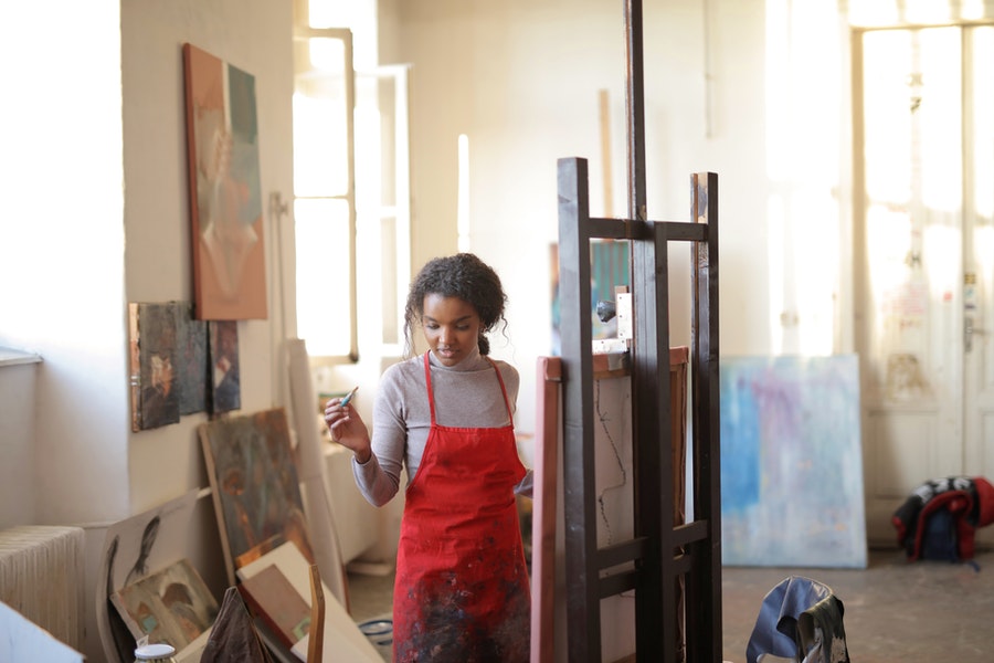 creative woman at an easel in a red apron, painting