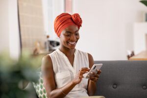 A woman sits on a couch smiling while looking at her phone