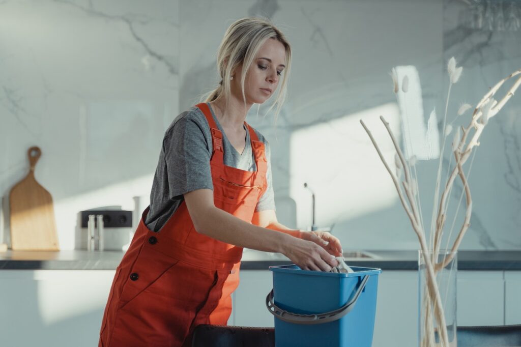 Woman in orange coveralls squeezing water out of a cloth and into a blue bucket