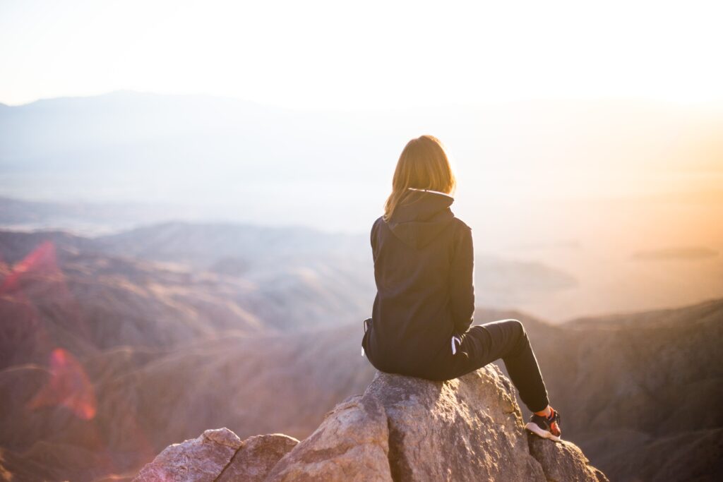 Woman sitting on top of mountaintop looking over other mountains.