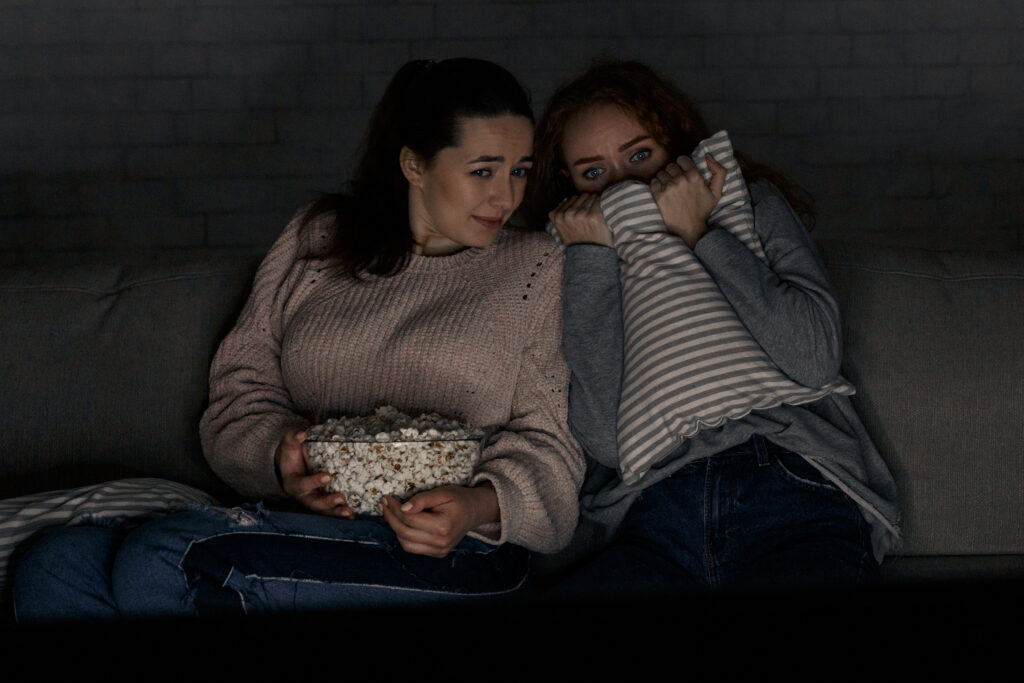 Teenage girls watching horror movie with popcorn, resting at home late in the evening