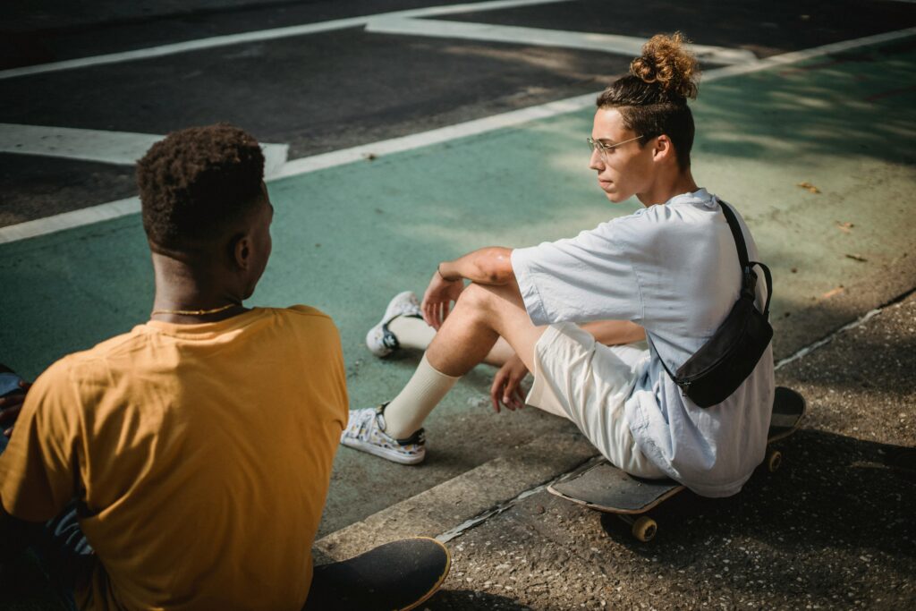 Two friends sitting on skateboards talking outside.